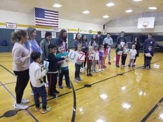 The high school students asked the kindergartners to come hold the alphabet signs with them.