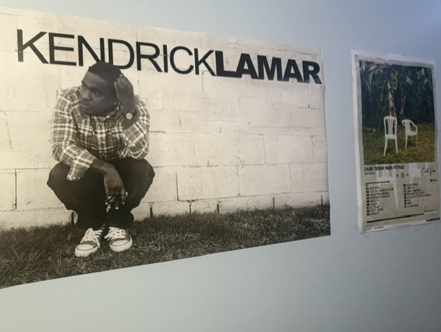 Two posters hang on a wall. One is of Kendrick Lamar, who uses his albums to connect to younger generations dealing with gang violence in an effort to help them cope with their situation and escape becoming trapped in the cycle and falling victim to a dangerous lifestyle. To the poster’s right is another poster for Bad Bunny’s album, "DeBÍ TiRAR MáS FOToS". Bad Bunny uses this album to create a sound that connects with not only Puerto Ricans, but also all people of Hispanic heritage. Both artists use their culture to connect with those who share that culture, using music to elevate their messages.